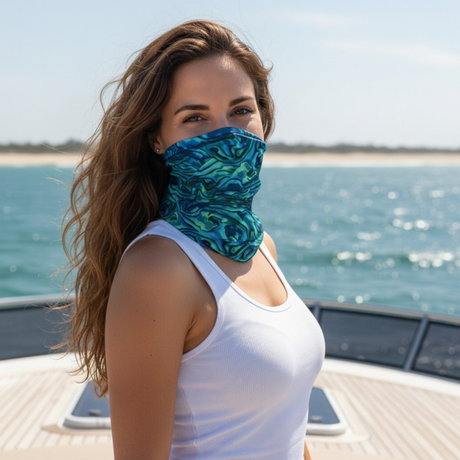 A woman on a boat wearing a teal and blue patterned neck gaiter mask, paired with a white tank top, with the ocean in the background.