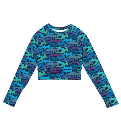 A long-sleeve crop top featuring an all-over repeating pattern of stylized shark silhouettes in shades of blue, teal, purple, and gray on a dark background.