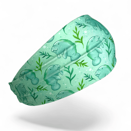 A mint green athletic headband featuring a repeating pattern of manatees and green seaweed on a white background.