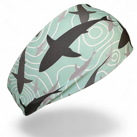 A fabric headband featuring a shark pattern on a mint green background, shown floating against a white background with a soft shadow underneath.