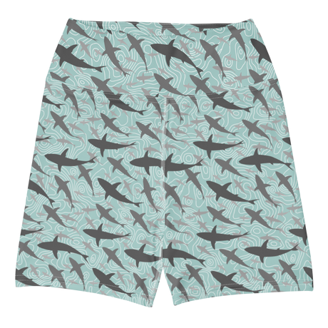 A pair of women's athletic shorts featuring an all-over print of swimming sharks on a light teal background with wavy contour lines.