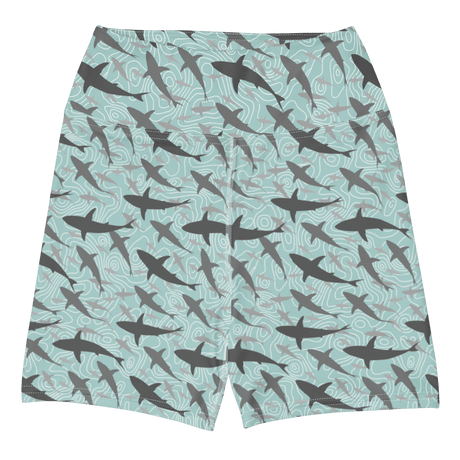 A pair of women's athletic shorts featuring an all-over print of swimming sharks on a light teal background with wavy contour lines.